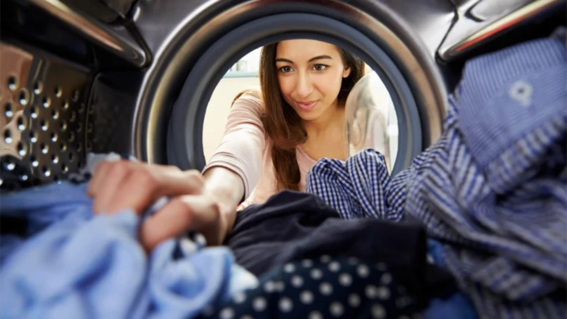 een afbeelding van een vrouw die kleren in de wasmachine doet