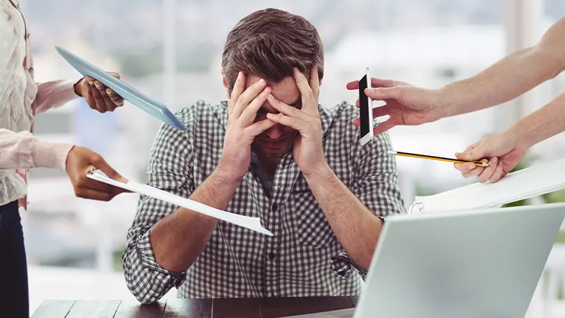 Een beeld van een man die wordt bedolven onder mensen die papieren en telefoons bij zijn hoofd leggen