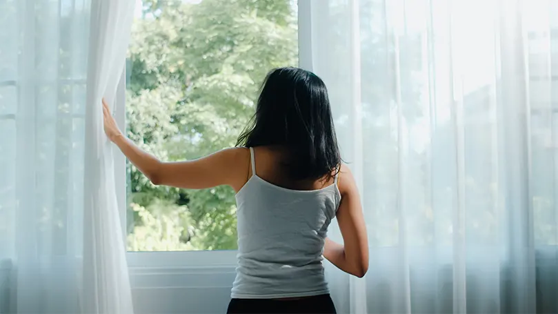 Een afbeelding van een vrouw die het raam opent en frisse lucht binnenlaat