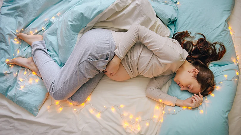 een afbeelding van een zwangere vrouw slapend in een bed met het licht aan