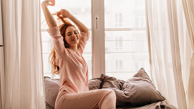 een vrouw in pyjama rekt zich uit voor een raam