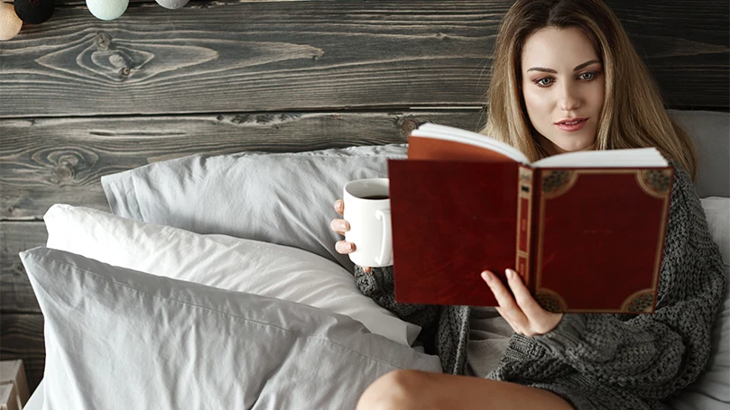 Een afbeelding van een vrouw die een boek leest in bed