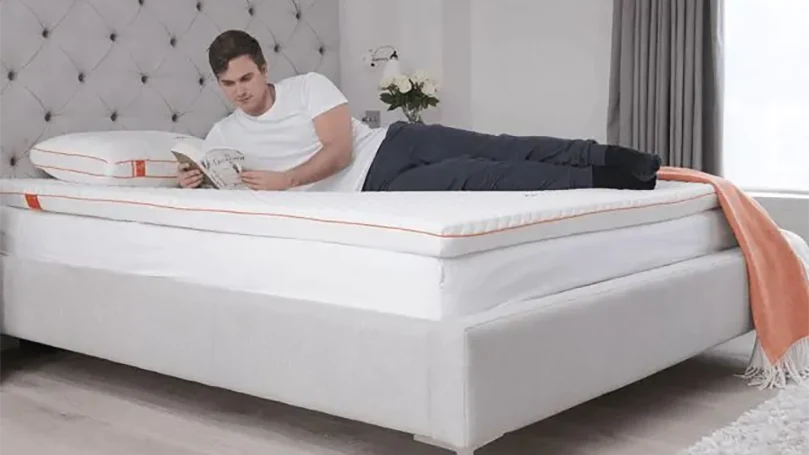 Een man ligt op de Dormeo Octasmart matras topper een boek te lezen.