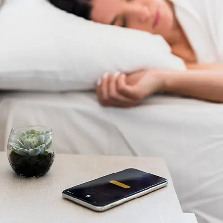 Een afbeelding van een vrouw die slaapt met haar telefoon op het nachtkastje