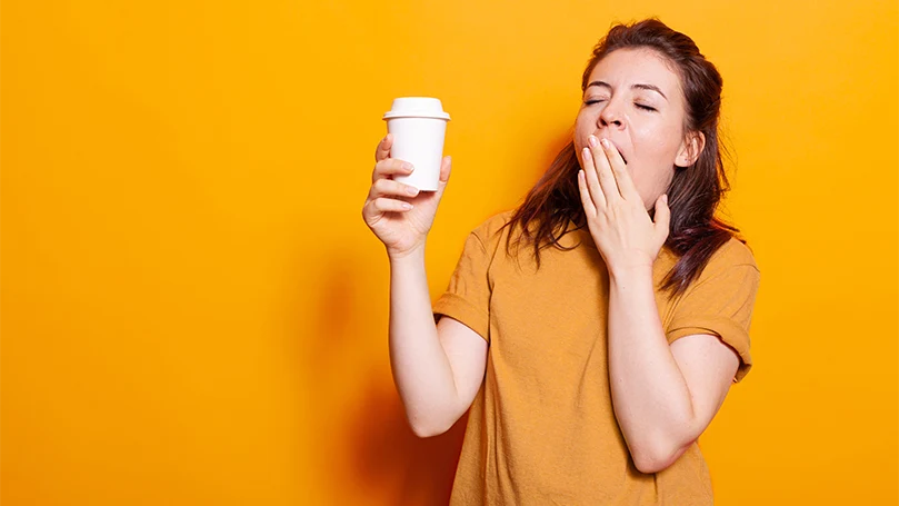 Een slaperige vrouw met een kop koffie in haar hand.