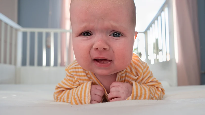 Een afbeelding van een huilende baby in een ledikant.