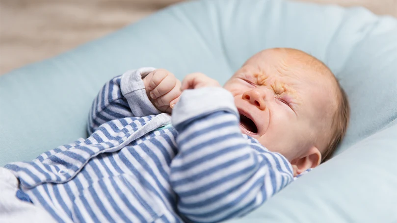 Een afbeelding van een huilende baby in een matras voor een ledikant.