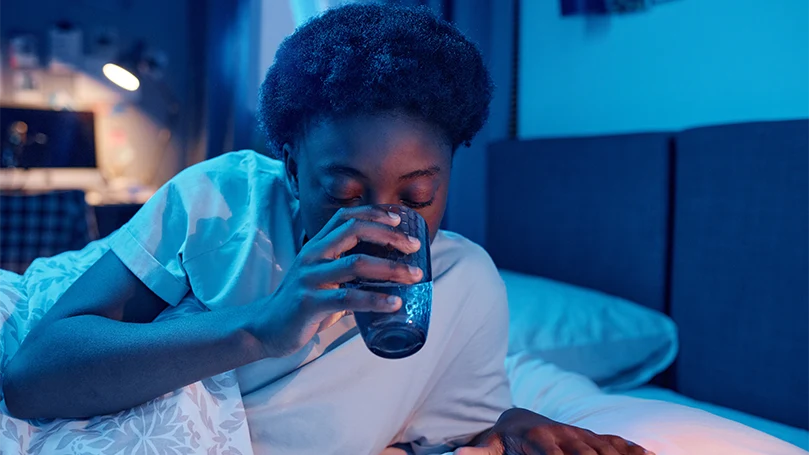 Een afbeelding van een vrouw die een glas water drinkt voor het slapen gaan.