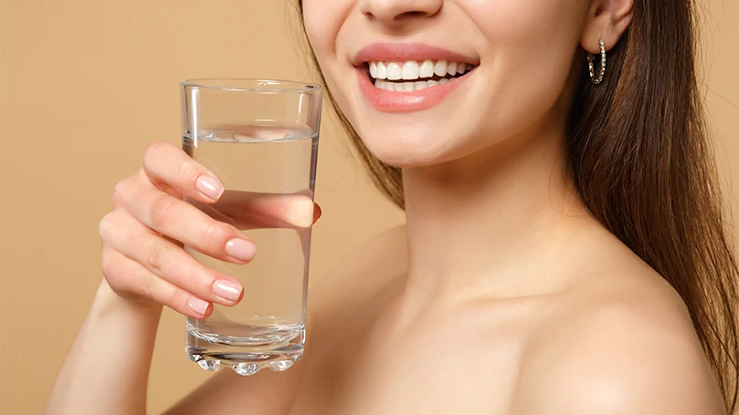 Een afbeelding van een vrouw die een glas water vasthoudt.