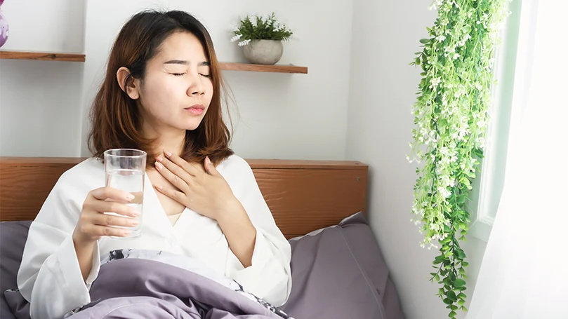 Een beeld van een jonge en zieke Aziatische vrouw die water drinkt in bed voordat ze gaat slapen.