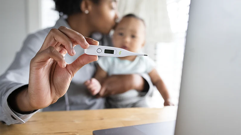 Een afbeelding van een moeder met haar baby met een thermometer