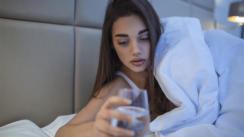 Een afbeelding van een jonge vrouw met een glas water in bed.