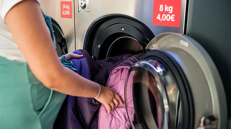 Een afbeelding van een zwangere vrouw die dekens in een wasmachine stopt.