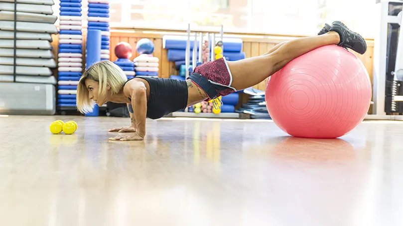 Een afbeelding van een vrouw die Decline pushups doet op een yogabal