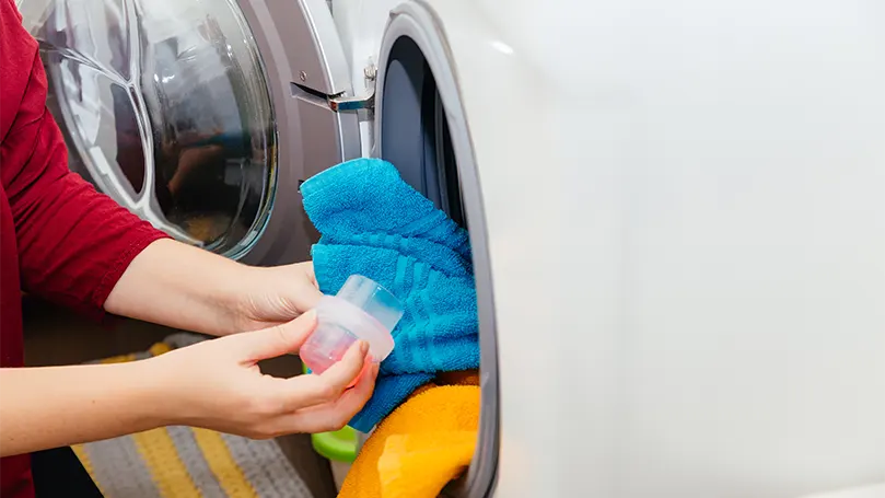 Een afbeelding van een vrouw die wasmiddel in een wasmachine giet.