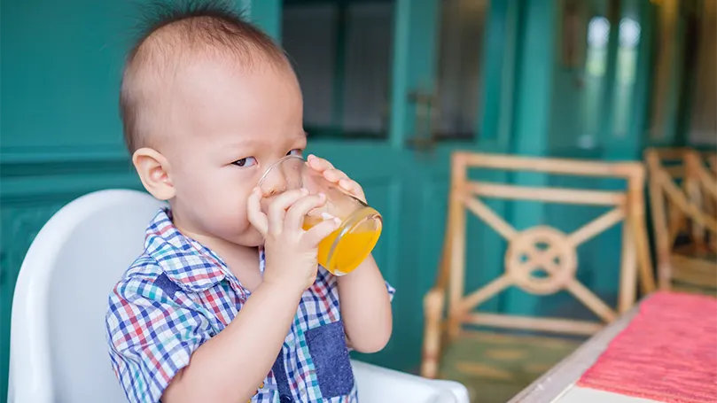 Een afbeelding van een 18 maanden oude baby die sap drinkt.