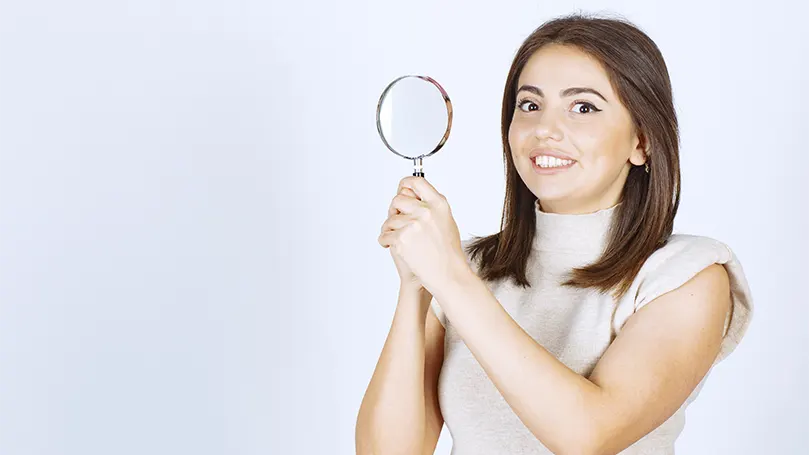 Een afbeelding van een jonge vrouw die een vergrootglas vasthoudt.