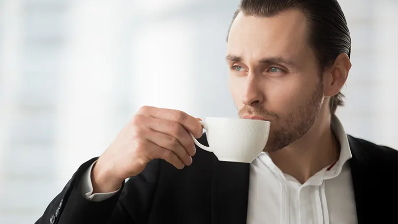 Een afbeelding van een man die koffie drinkt en aan het dagdromen is.