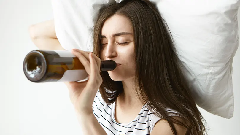 Een afbeelding van een vrouw die alcohol drinkt in bed.