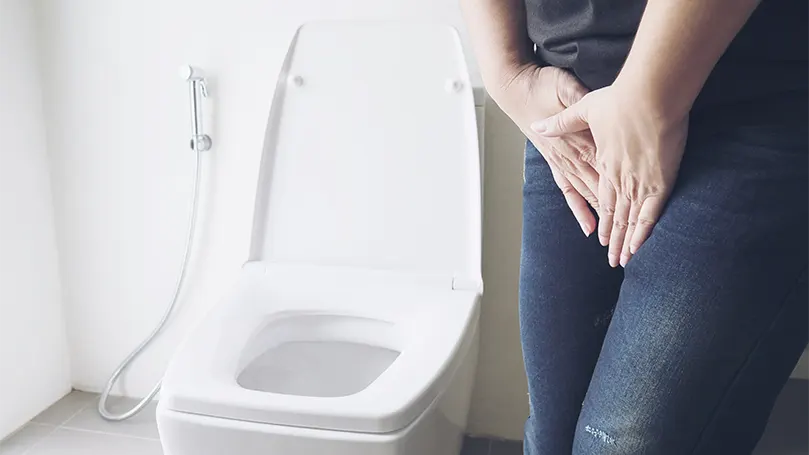 Een afbeelding van een vrouw die haar blaas ophoudt omdat ze moet plassen naast het toilet.