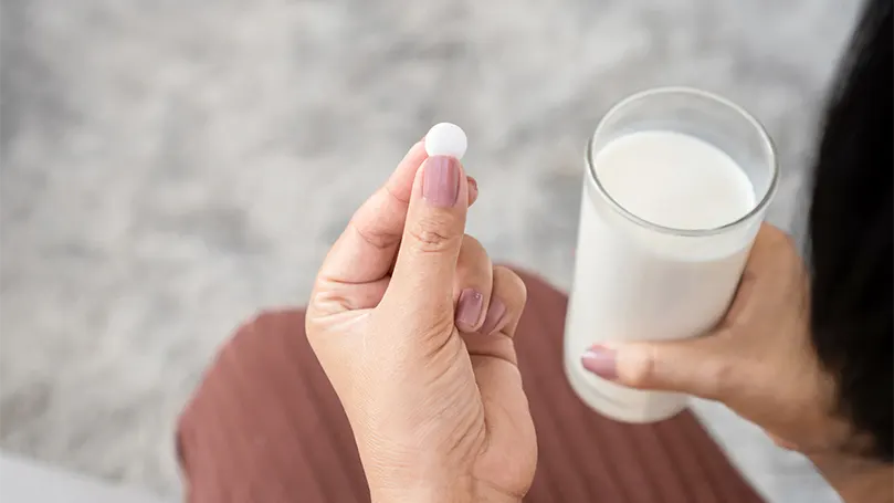 Een vrouw neemt een melatoninepil met een glas melk.