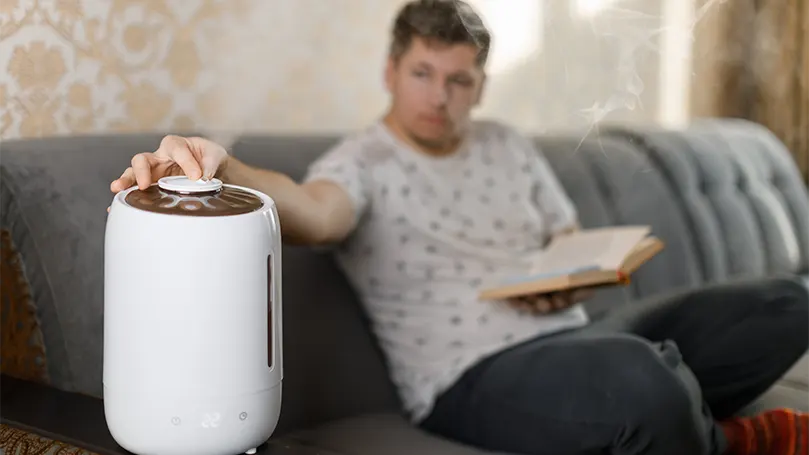 Een jonge man leest een boek op een bank en zet een humidifer op