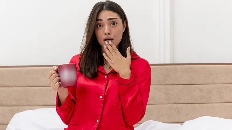 Een afbeelding van een vrouw in rode pyjama die water drinkt omdat ze wakker wordt van een droge mond.