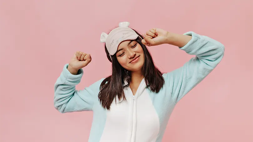 Een afbeelding van een jonge Aziatische vrouw in een zachte pyjama met slaapmasker.