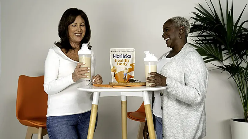 Twee vrouwen houden glazen horlicks vast en staan naast een tafel