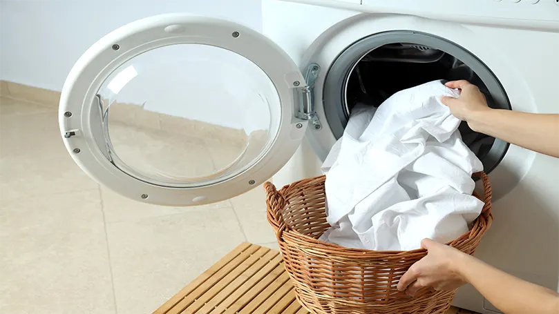 een vrouw die witte lakens in een wasmachine doet.