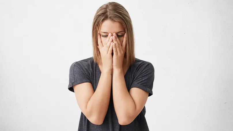 Een afbeelding van een vrouw met haar handen over haar gezicht terwijl ze lijdt aan symptomen van wintermoeheid