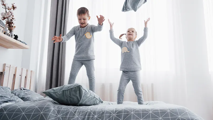 Een afbeelding van twee jonge kinderen die op het bed springen.