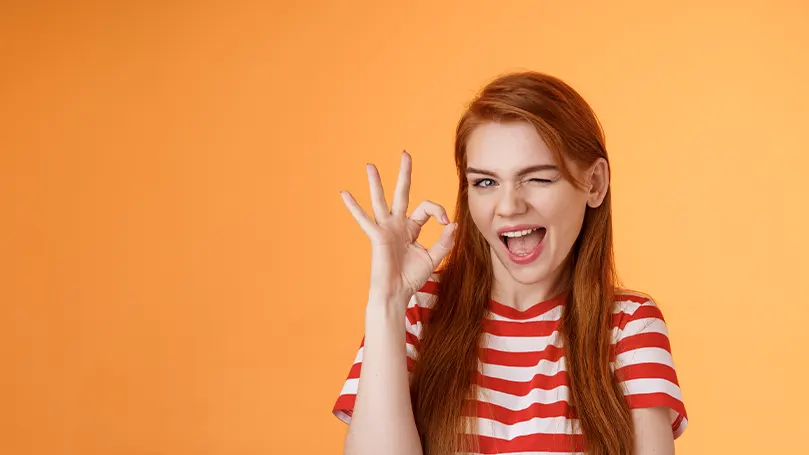 Een afbeelding van een vrouw die knipoogt en met haar hand een 'ok'-teken toont.