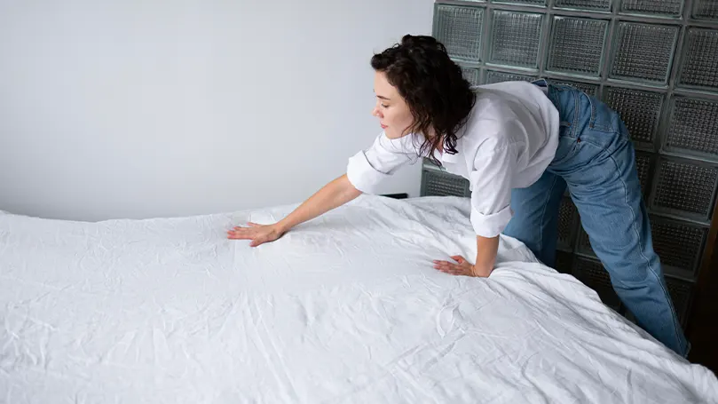 Een afbeelding van een vrouw die haar bed opmaakt.