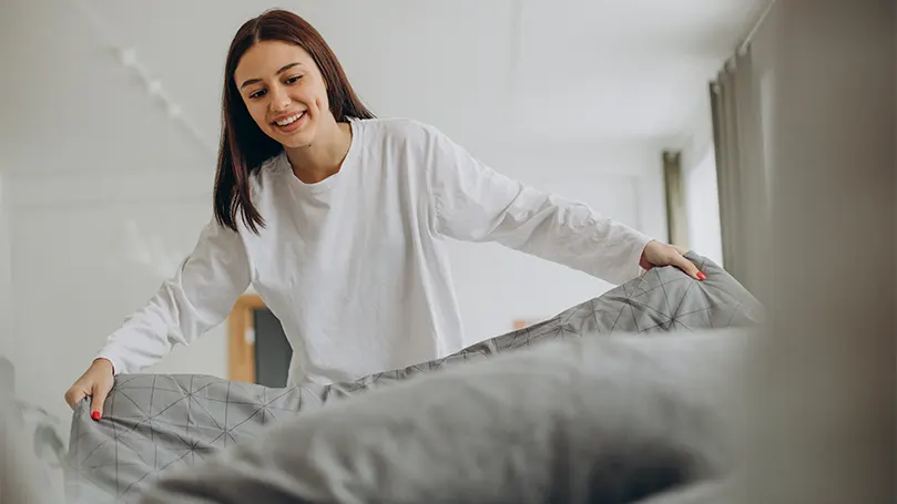 Een afbeelding van een gelukkige vrouw die haar bed opmaakt.