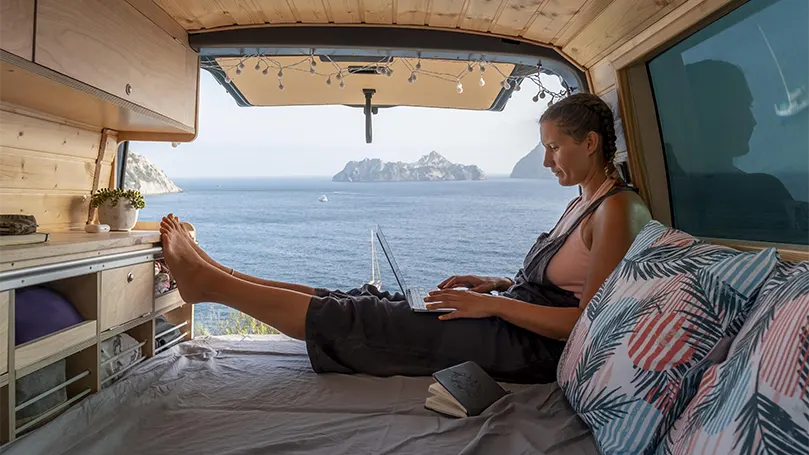 Een afbeelding van een jonge vrouw zittend op een matras in een kampeerbusje