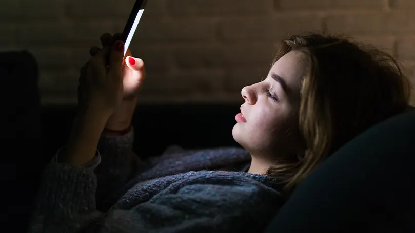 Een afbeelding van een meisje dat in bed naar haar telefoon kijkt