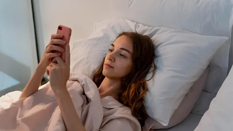 Een afbeelding van een jonge vrouw in bed die een telefoon vasthoudt