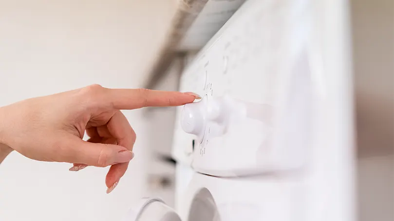 Een afbeelding van een vrouw die een wasmachine aanzet