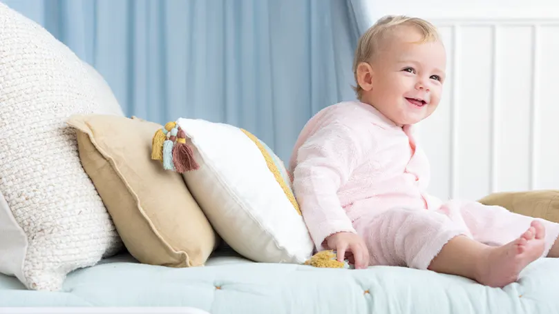 Een afbeelding van een kind zittend op een bed naast een paar peuterkussens