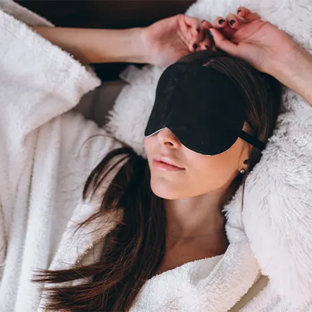 Een afbeelding van een vrouw in bed met een slaapmasker