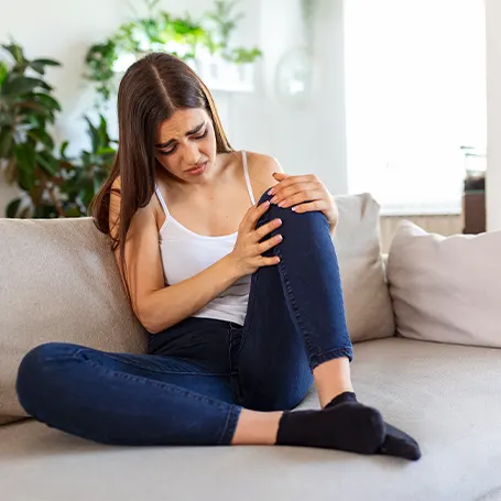 Een afbeelding van een vrouw met pijn in haar been die haar knie vasthoudt