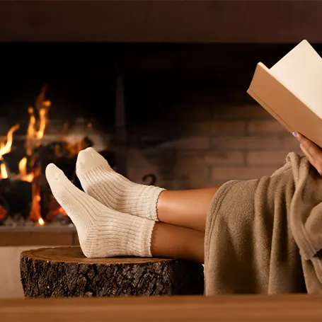 Een afbeelding van een persoon die een elektrische deken gebruikt en een boek leest voor een open haard