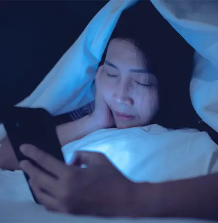 Een afbeelding van een vrouw in bed die naar haar telefoon kijkt